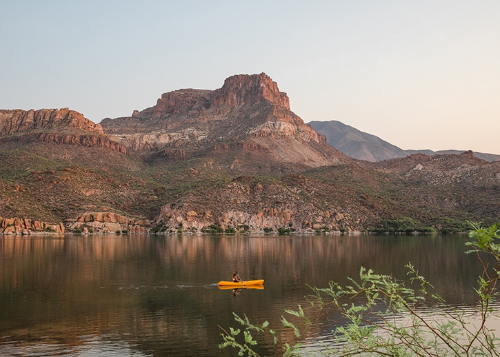 One woman in a yellow cayak on Apache Lake's calm waters.