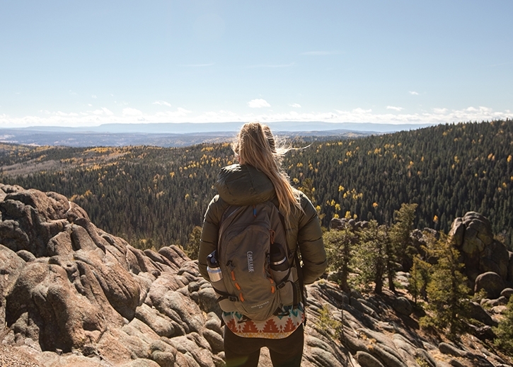 A blonde woman views over a summit on the East Baldy Trail.