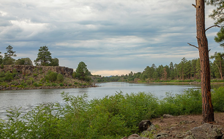 Clouds fill the sky over a green forest and smooth lake waters below.