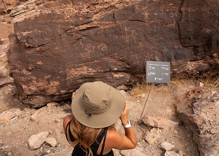 A woman in a hat takes a photo of petroglyphs at Homolovi State Park.