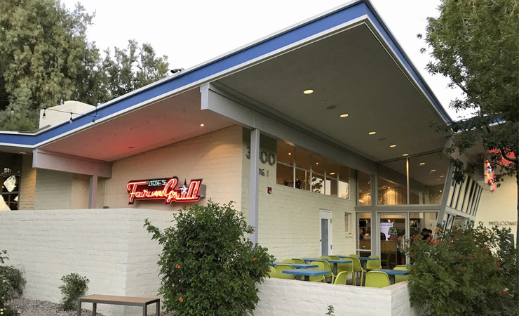 Exterior of a mid-century-modern building in white. A neon sign displays the name 'Joe's Farm Grill'.