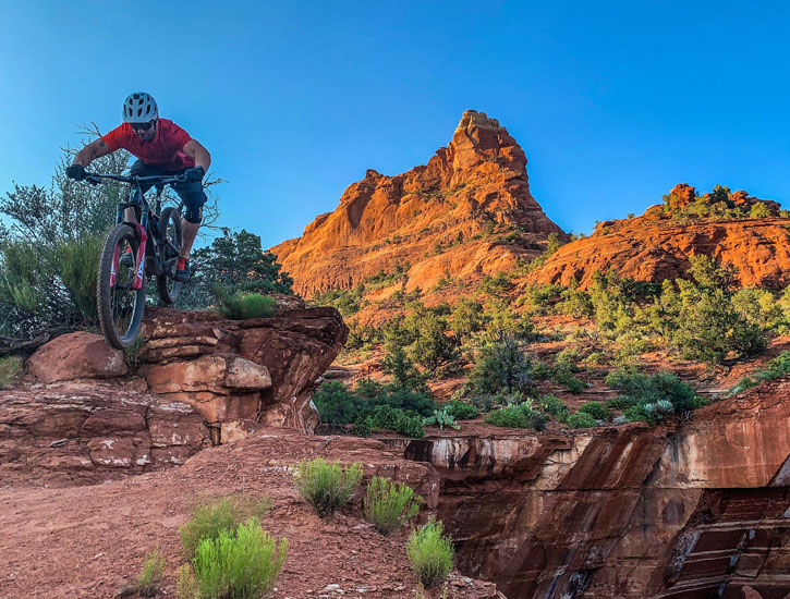 A mountain biker leaps over a rocky hill, a large mountain behind him