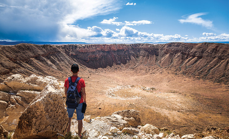 A man stands at the edge of a massive crater