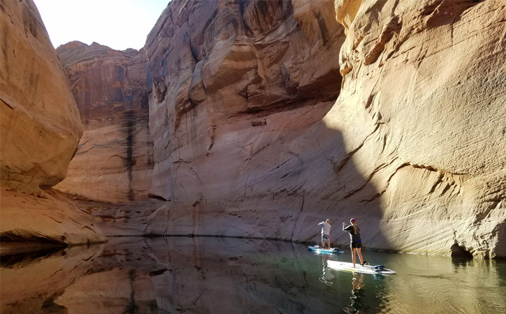 Two paddleboarders make their way through a canyon, partially covered in shadows