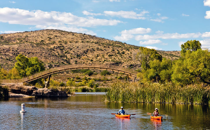 Kayakers sail along near an arched bridge that mimics the curves of the hills behind them.