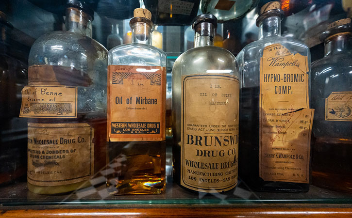 Four vintage bottles of medicine are lined up on a shelf, with yellow, peeling labels