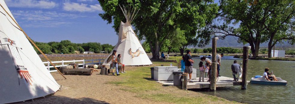 A group of family and friends play in the lake near the teepees and trees and Jackpot Ranch.