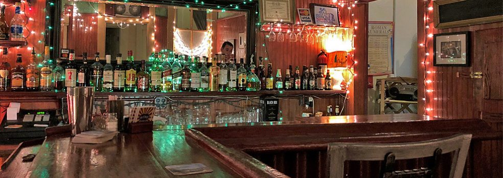 Bottles line the back of a bar, which is decorated with red and green Christmas lights