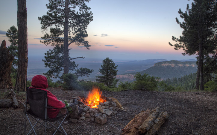 A man sits near a small campfire overlooking the Grand Canyon