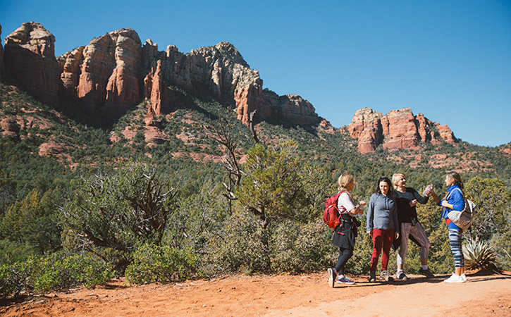 A group of women chat on a desert trail beside a landscape of red rocks