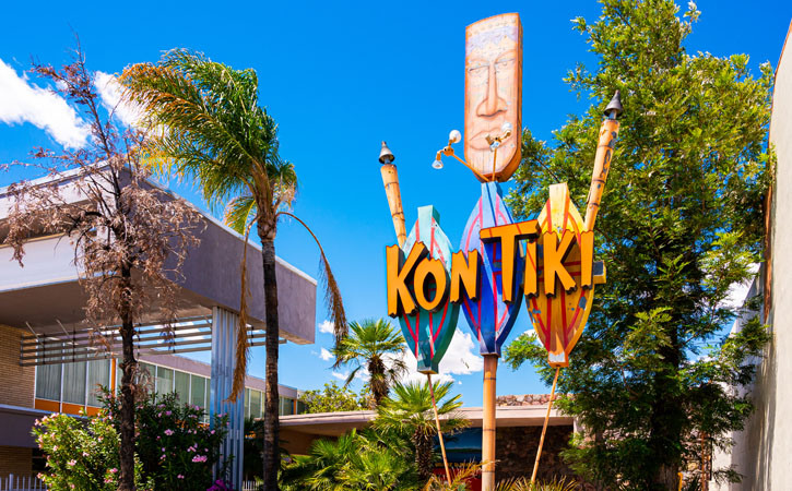 A large sign saying 'kon-tiki' in a Polynesian style stands outside a nondescript set of building next to several palm trees