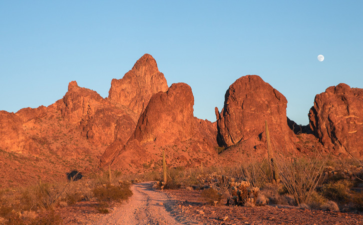 Red and orange-hued mountain peaks in the desert under a blue sky