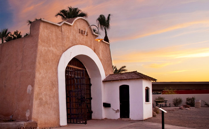 A historic, Spanish Mission-style building sits underneath a sunset-filled sky