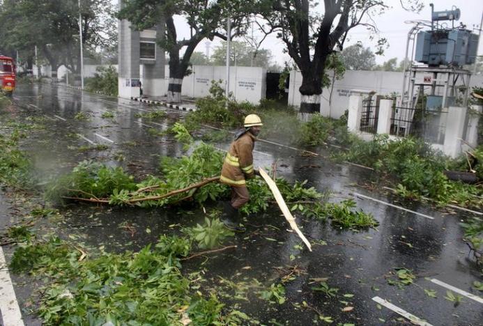 A rescue member removes a fallen branch of a tree that fell on a road after it was uprooted by strong winds in Chennai