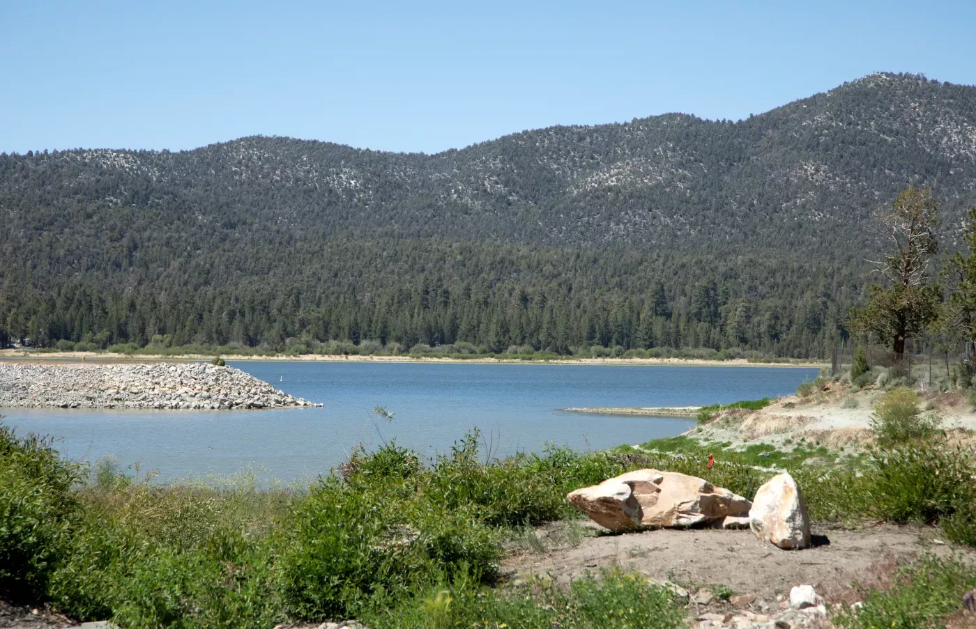 View of Big Bear Lake with forested mountains and large rocks in the foreground