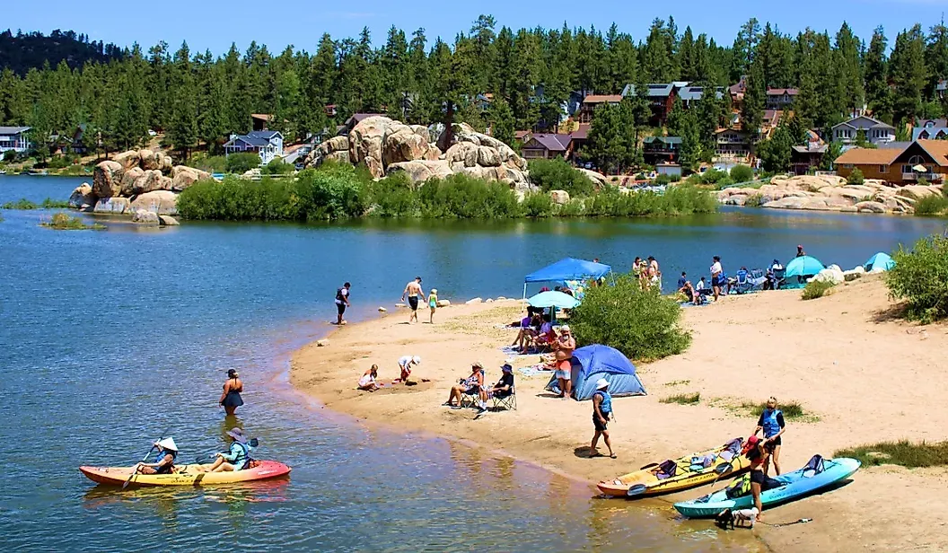 Many families gathered, relaxing along the lakeside beach, up close are kayakers getting ready to go out onto the water.