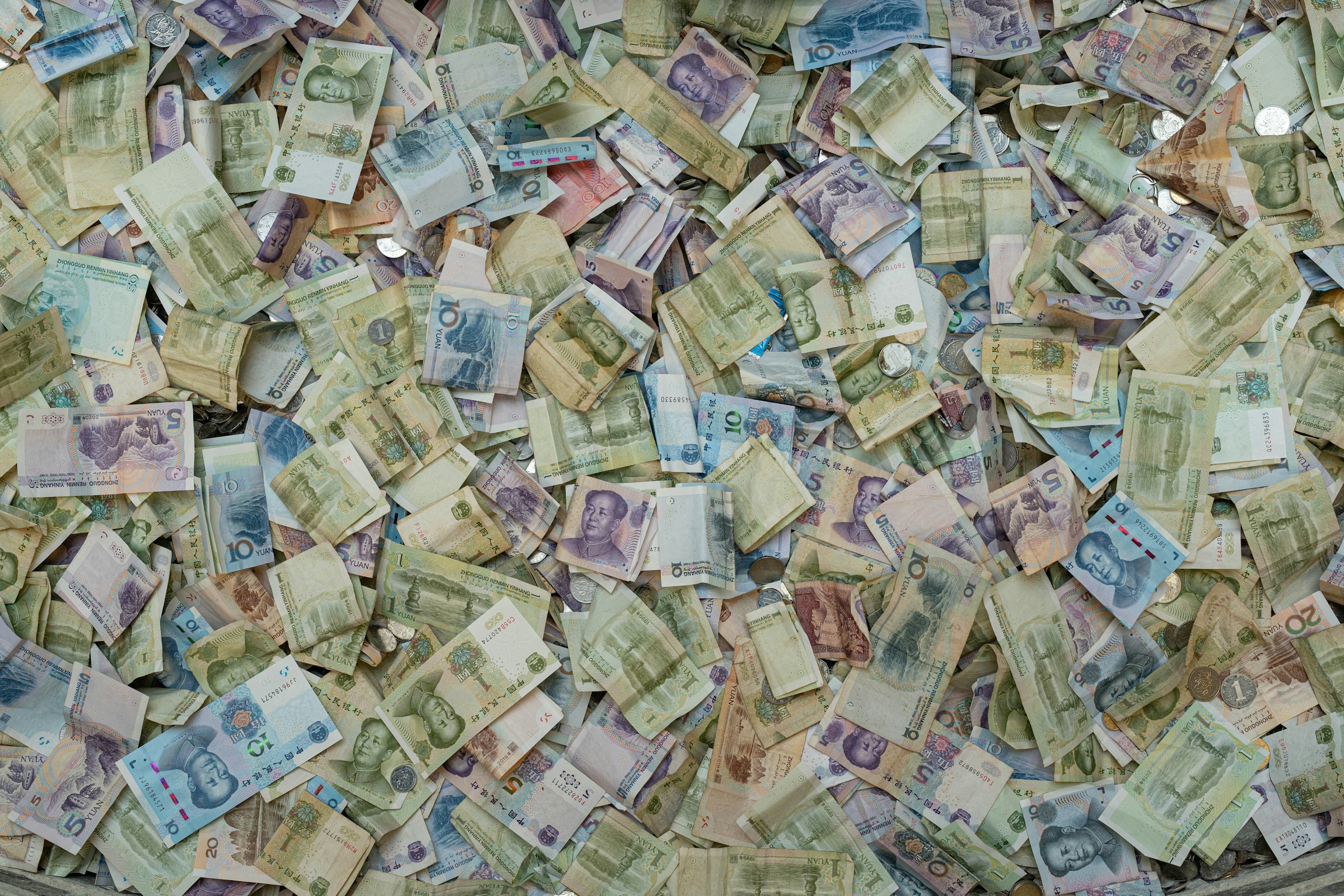 A large pile of various denominations of Chinese yuan banknotes and a few coins, possibly indicative of hidden assets, scattered on a flat surface.
