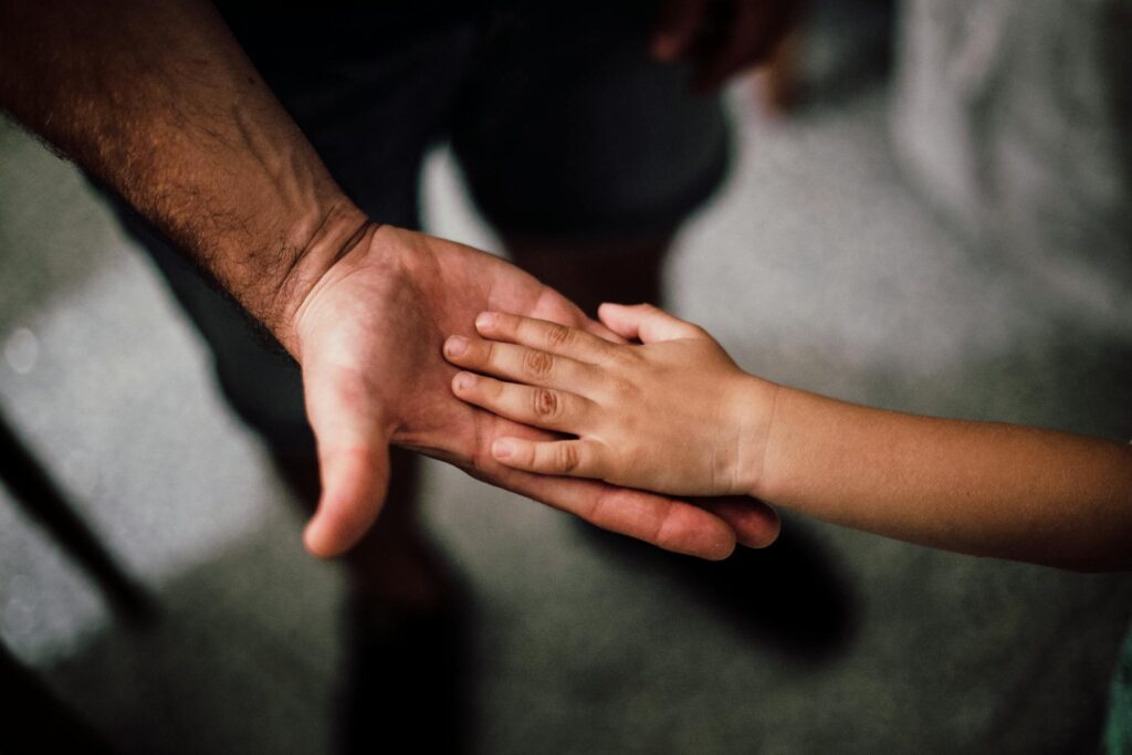 A child's hand resting on top of an adult's open palm, both hands facing upward on a neutral background—symbolizing support and guidance through California child support modifications and requirements.