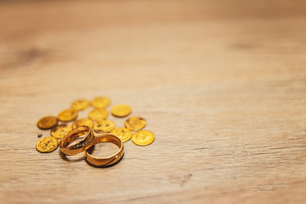 Two gold rings and several small gold coins, often representing retirement savings, are placed on a wooden surface in California.