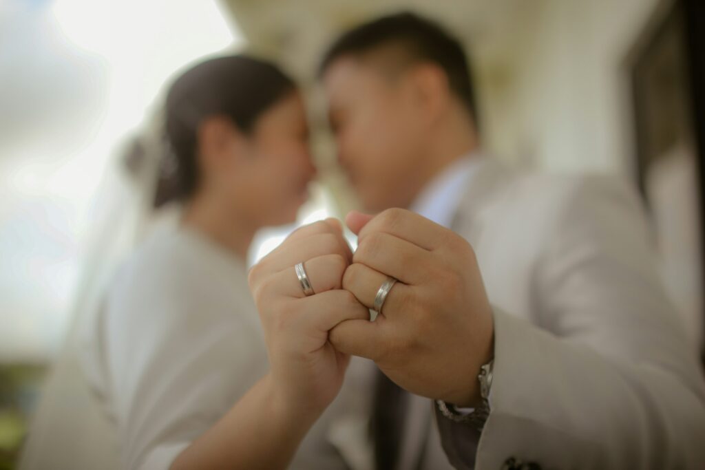 A couple wearing wedding rings holds hands with interlocked pinkies; their faces are out of focus and close together in the background, hinting at their bond despite challenging times, such as facing an unfair prenuptial agreement in California.