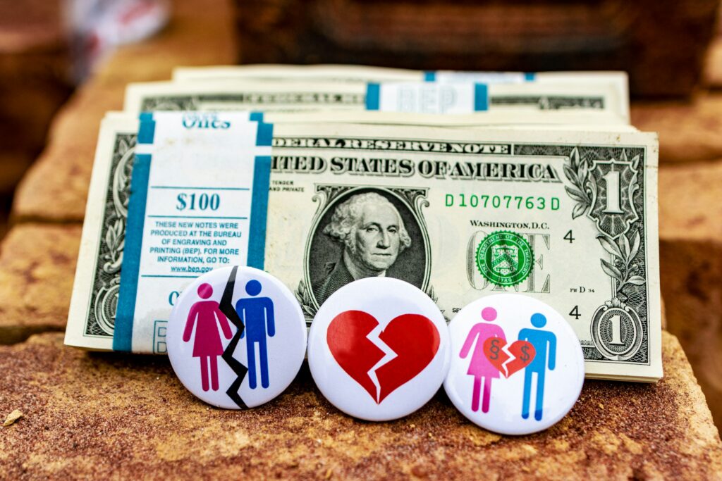 Three illustrated buttons depicting relationship and money themes are displayed in front of a stack of U.S. dollar bills, reflecting the financial complexities often seen in a high net worth divorce.