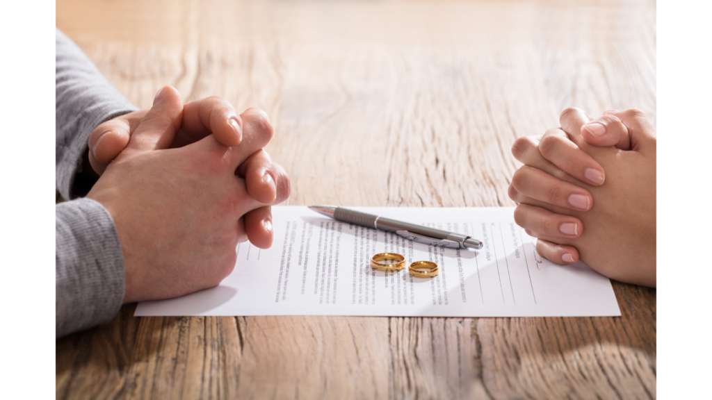 Why Divorce Outcomes Are Shaped Long Before You Ever Go to Court: A Guide to Key California Laws 1 Two people sit across from each other at a table with hands clasped, a pen, two wedding rings, and a document between them, contemplating divorce outcomes under California laws.