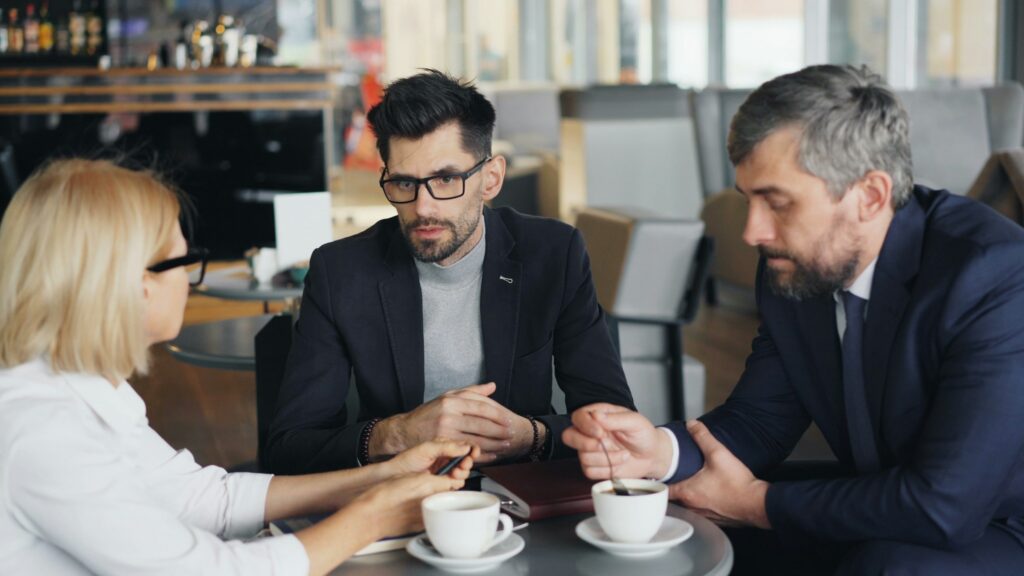 Three business owners in California, dressed in formal attire, sit at a café table engaged in a serious conversation about divorce over coffee cups.