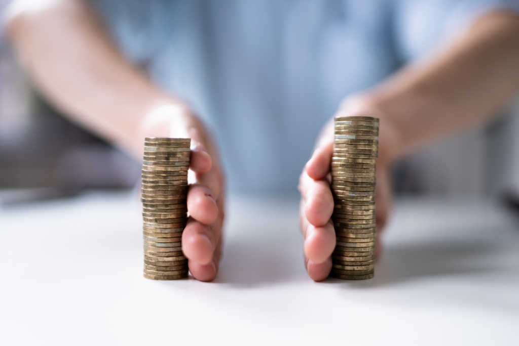 What Happens If One Spouse Controls All the Finances in a California Divorce? 1 A person separates two stacks of coins with both hands on a white surface, dividing the coins evenly—much like how finances are distributed during a California divorce when a spouse controls the assets.