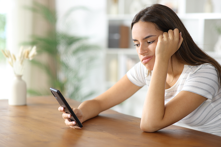 A pretty young Latina gazing at her phone and feeling dissatisfied and not knowing why