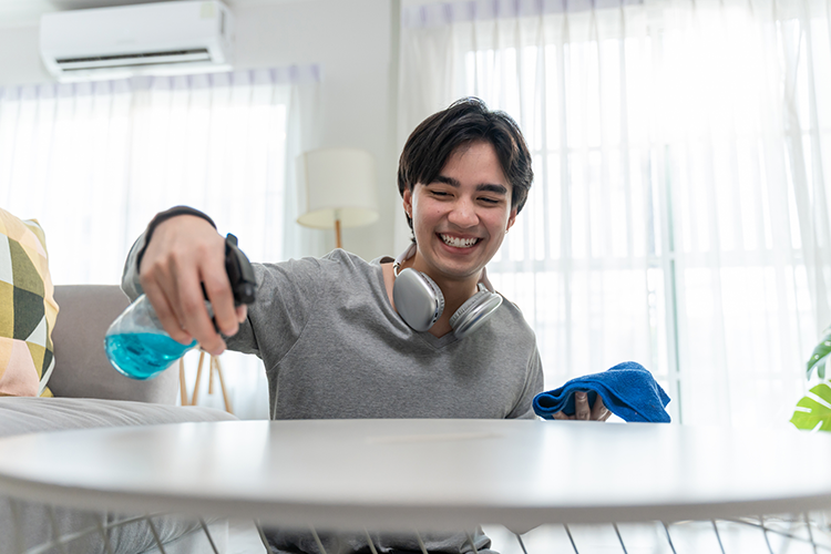 Image of a happy young Asian man cleaning and organizing his living room