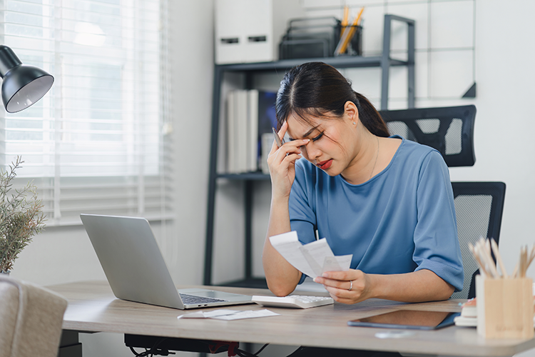 Picture of a young Asian woman watching financial news on her laptop and stressing over some purchase receipts