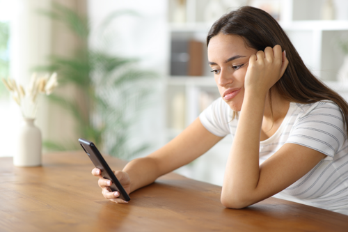 A pretty young Latina gazing at her phone and feeling dissatisfied and not knowing why
