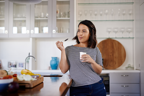 Picture of a young Latina eating yogurt in her kitchen for a stronger gut microbiome