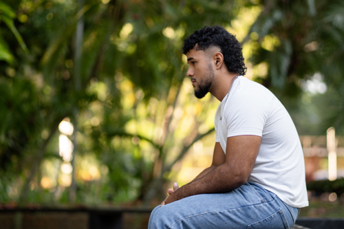 Young bearded hispanic man sitting on a park bench looking pensive and sad