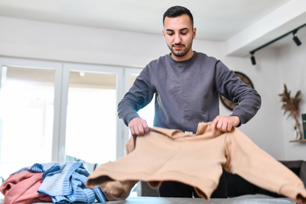 Image of a determined young Hispanic man folding and organizing his clothes