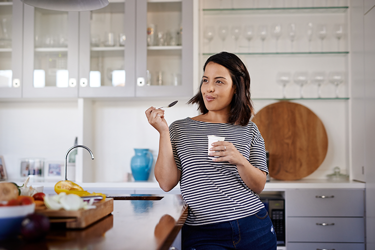 Picture of a young Latina eating yogurt in her kitchen for a stronger gut microbiome