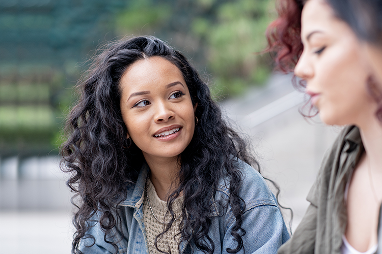 Two young women of different backgrounds sitting outside and talking about what they have in common