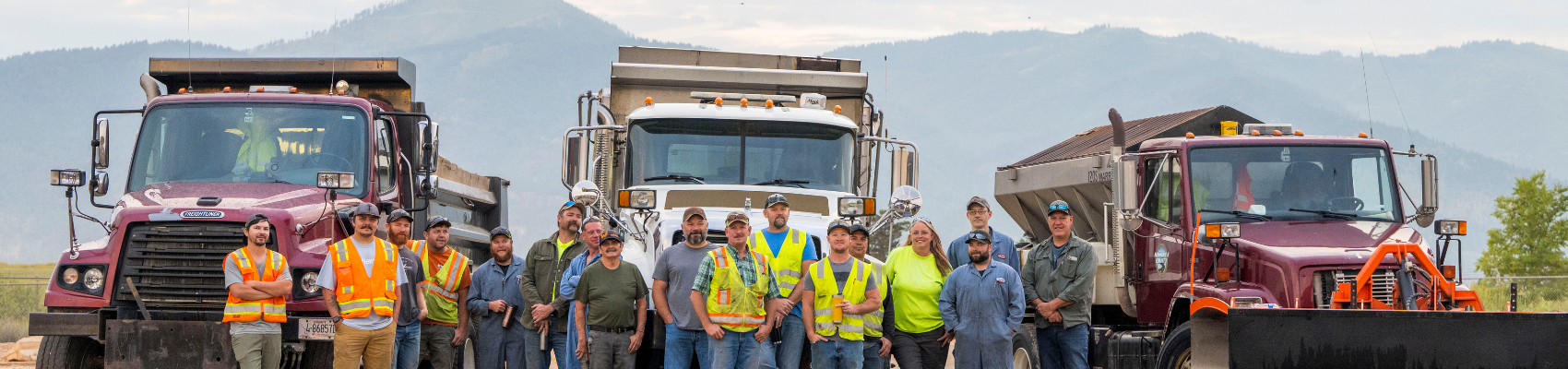 A color photo of Public Works staff wearing high-visibility vests, standing in front of large trucks and equipment.