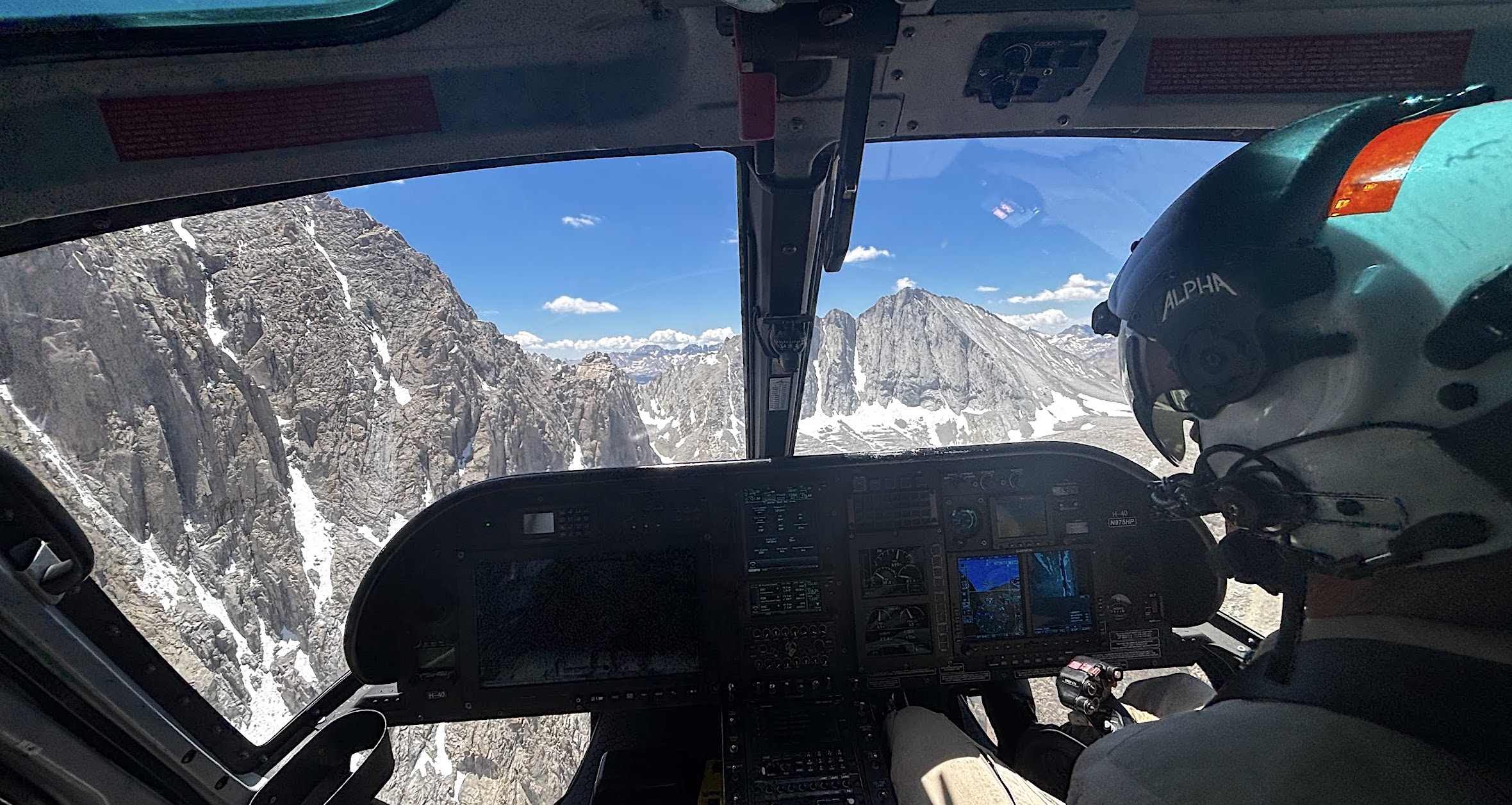 image of the view out the front of the cockpit of a helicopter with rocky mountain slopes out the window