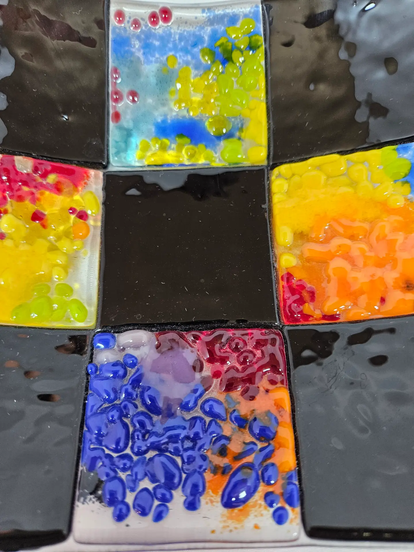 A close-up of Patchwork in Black 2 highlights a vibrant mosaic with blue, red, yellow, and orange tiles encircling a central black cross-like design.