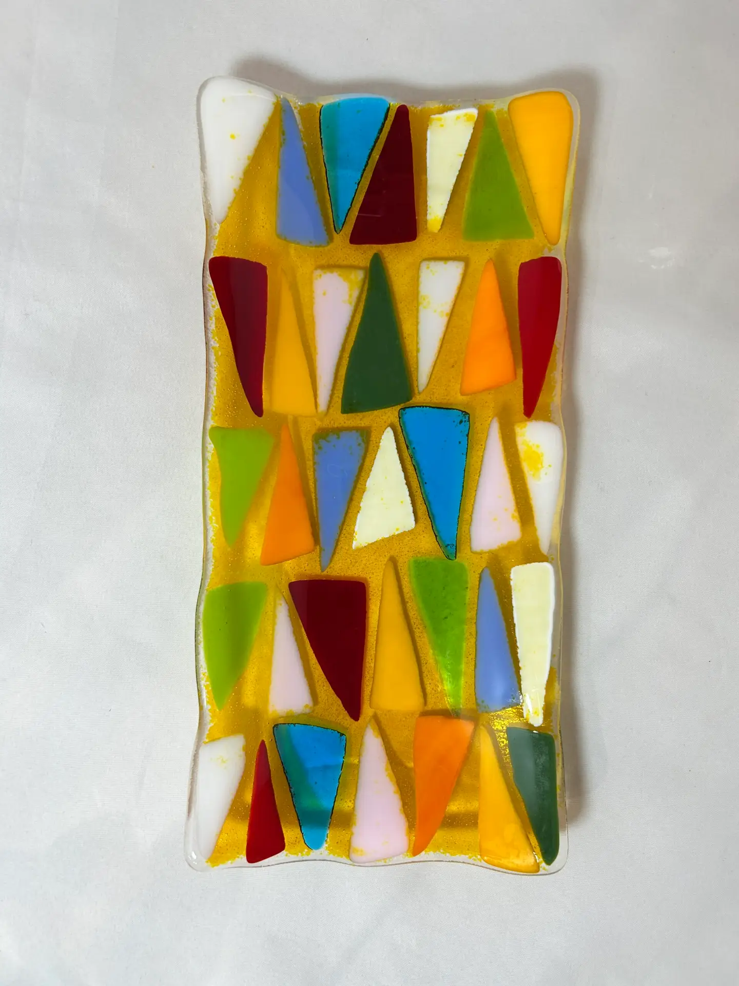 The Festival of Triangles is a rectangular glass art piece featuring colorful abstract triangular patterns in red, blue, orange, green, and white.