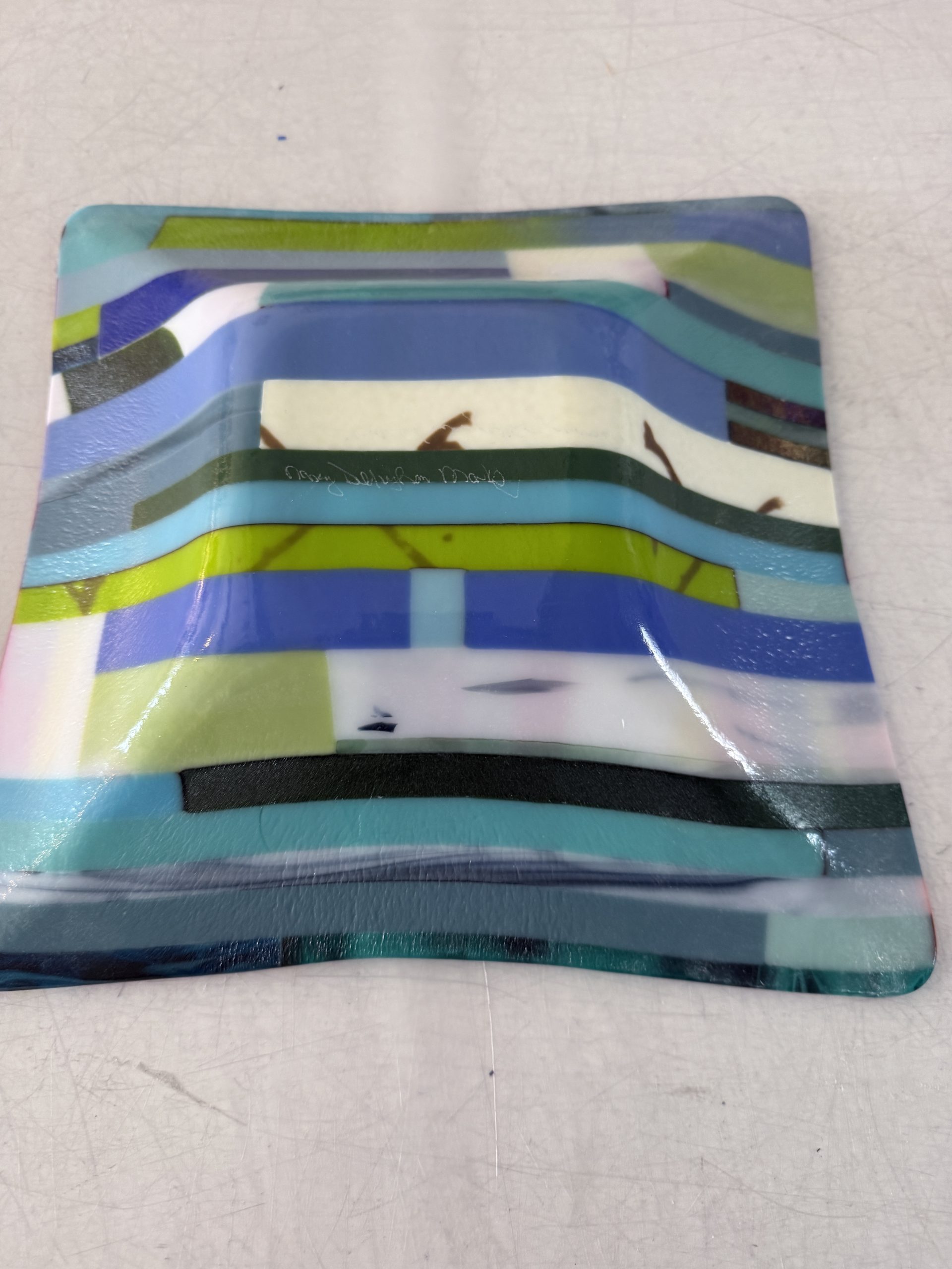 Square fused glass bowl showing layered blue and green stripes on the exterior, gently contoured shape with a glossy kiln-fired finish.