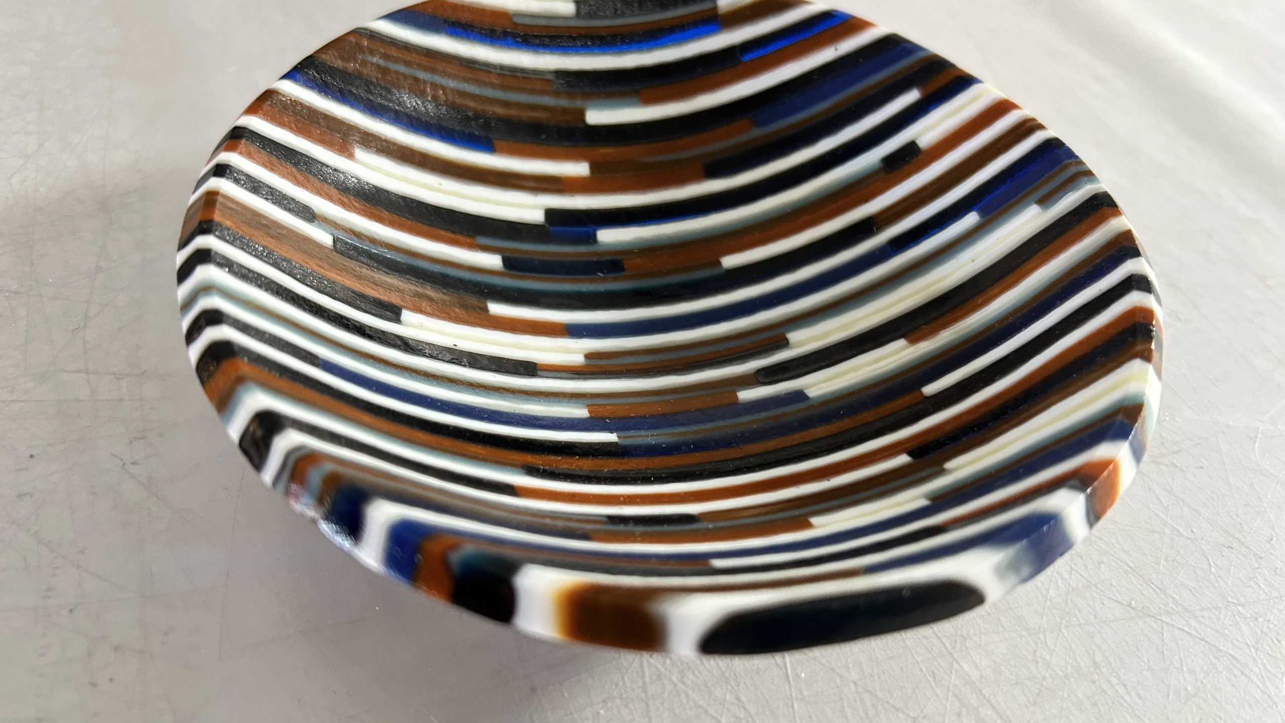 Strips of earthtone colored glass cut and assembled into a small bowl.