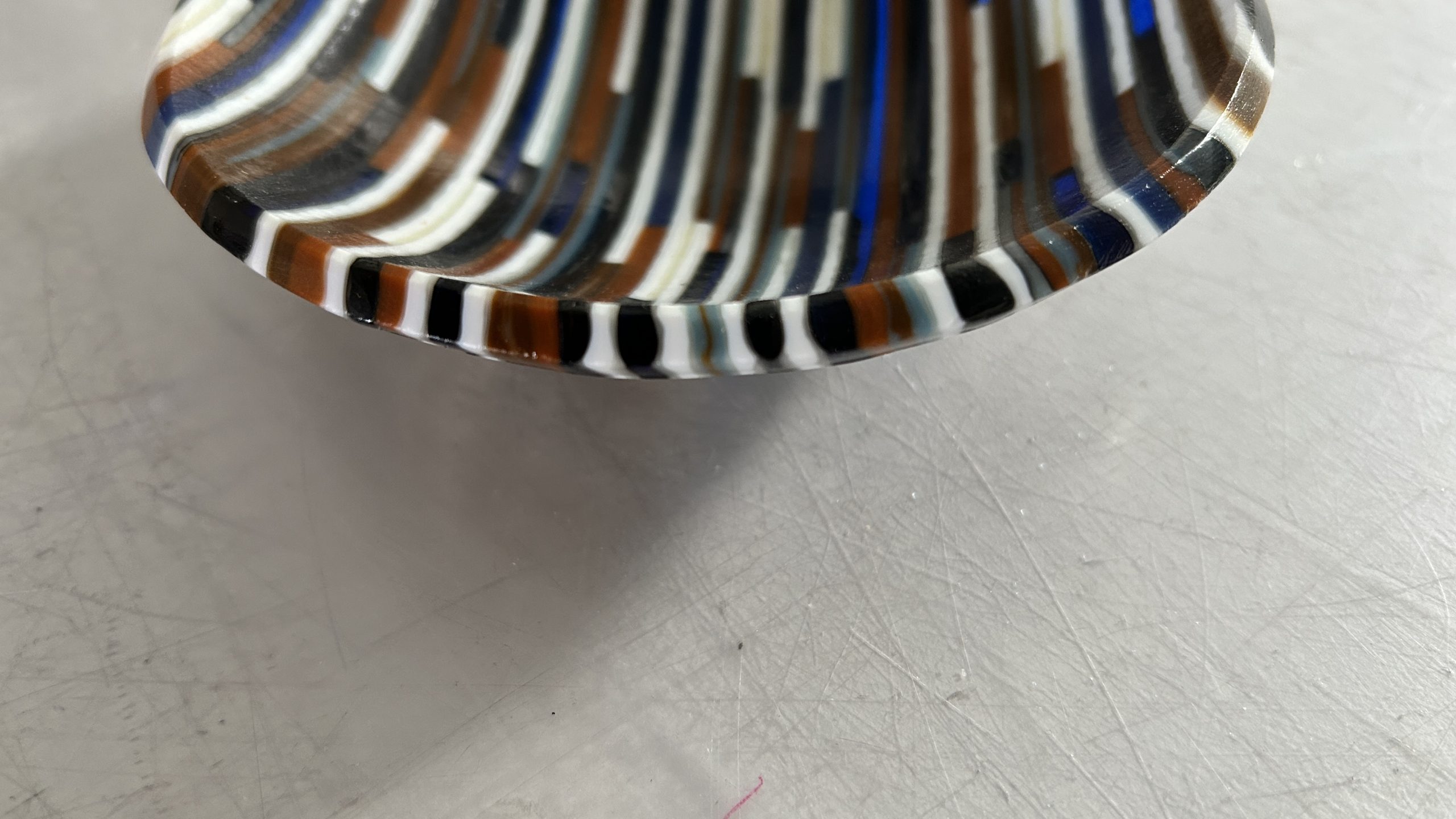 Strips of earthtone colored glass cut and assembled into a small bowl. Looking at the edge of the bowl at the wonderful colors