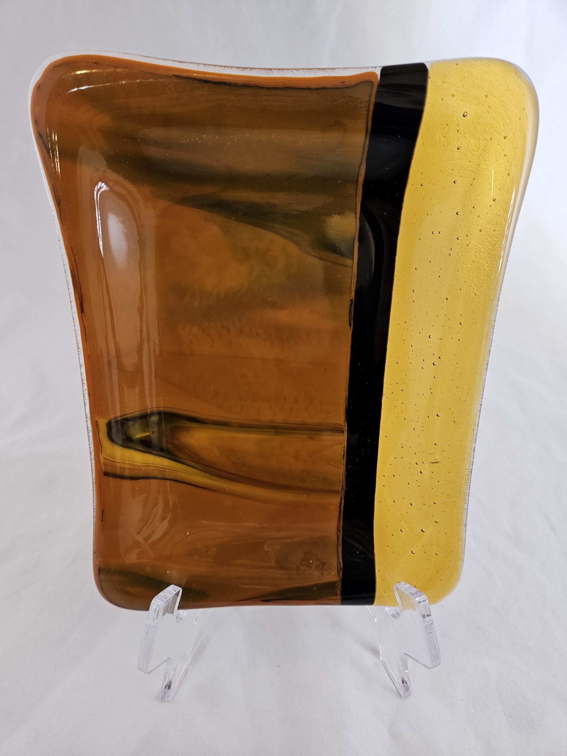 Handmade fused glass plate featuring warm amber tones and bold black linear detail