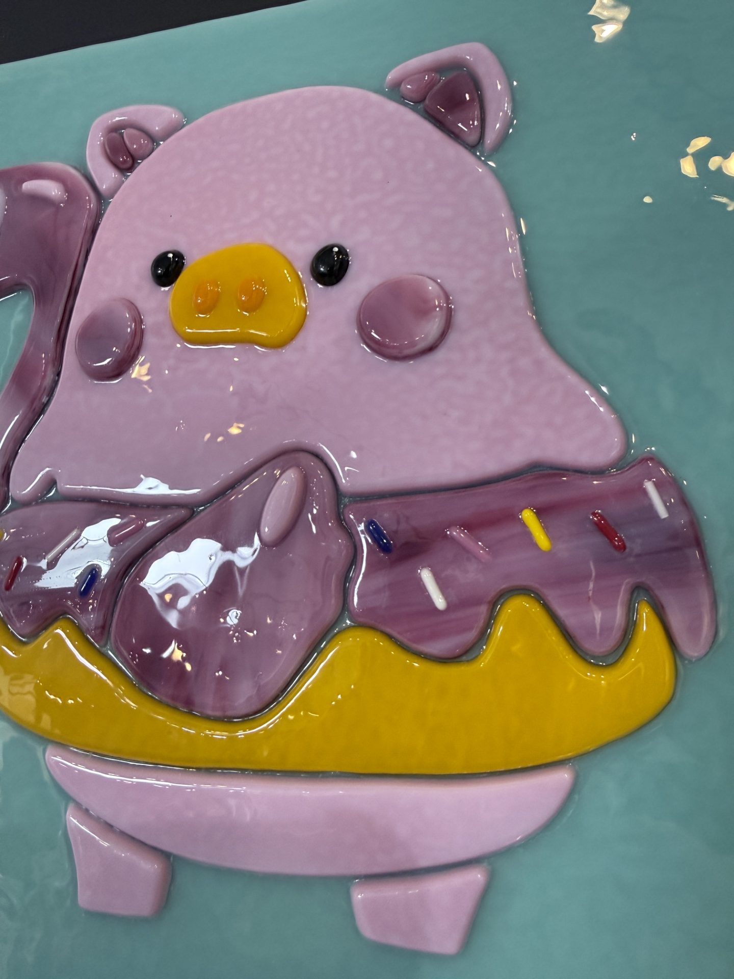 Close-up of Lulu the Pig fused glass commission with pink face and yellow snout