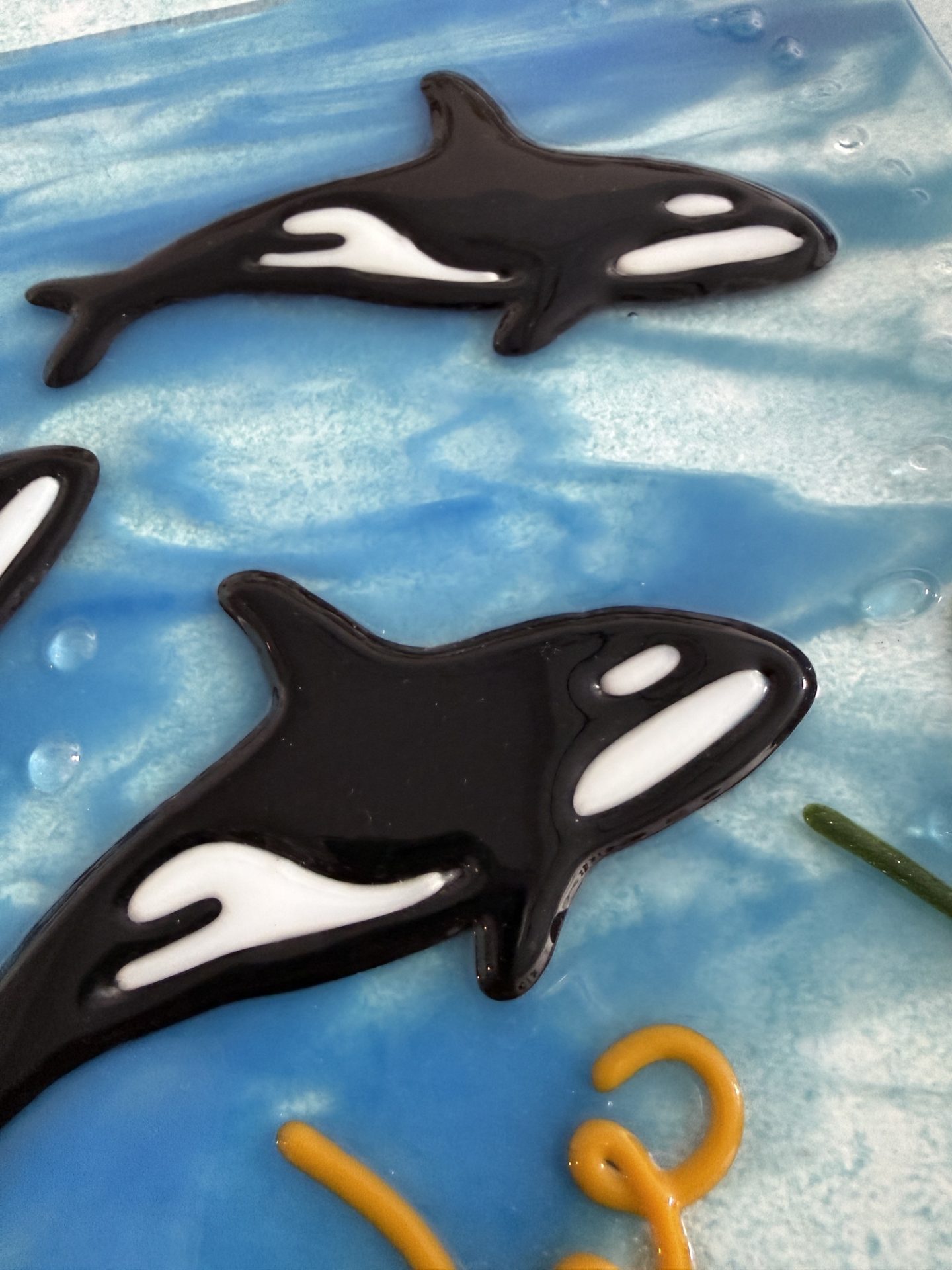 Close-up of handcrafted black-and-white glass orcas in Ocean Kin by Linda Simmon