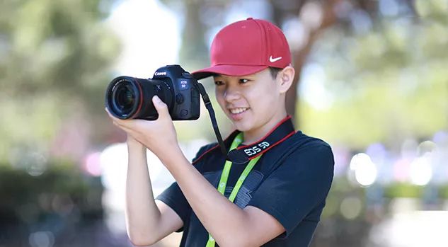boy in red hat holding camera and looking through it