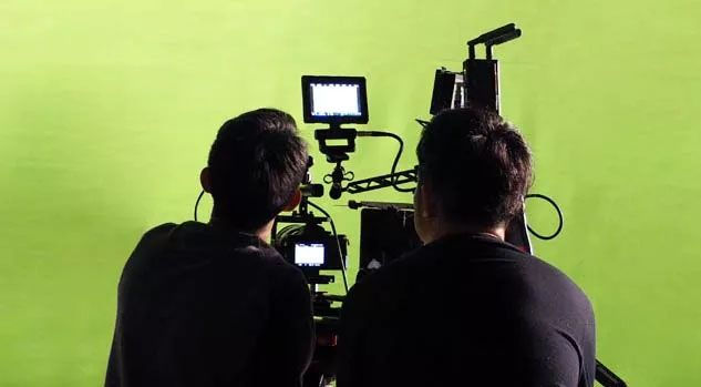 two students looking through camera at greenscreen