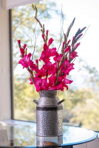 Pink Gladiolus arranged in a metal vase with curly willow twigs